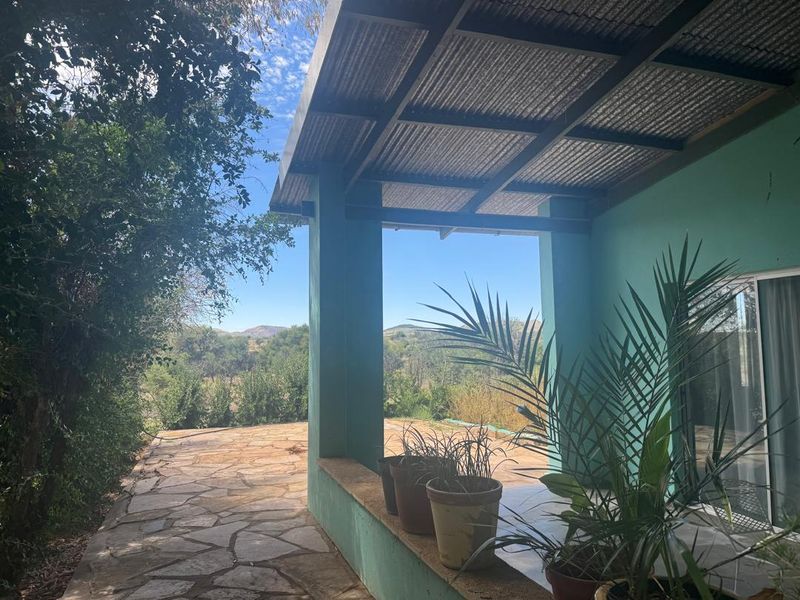 A covered outdoor patio featuring stone paving, masonry pillars, and a built-in bench, offering scenic views of the surrounding farm landscape.