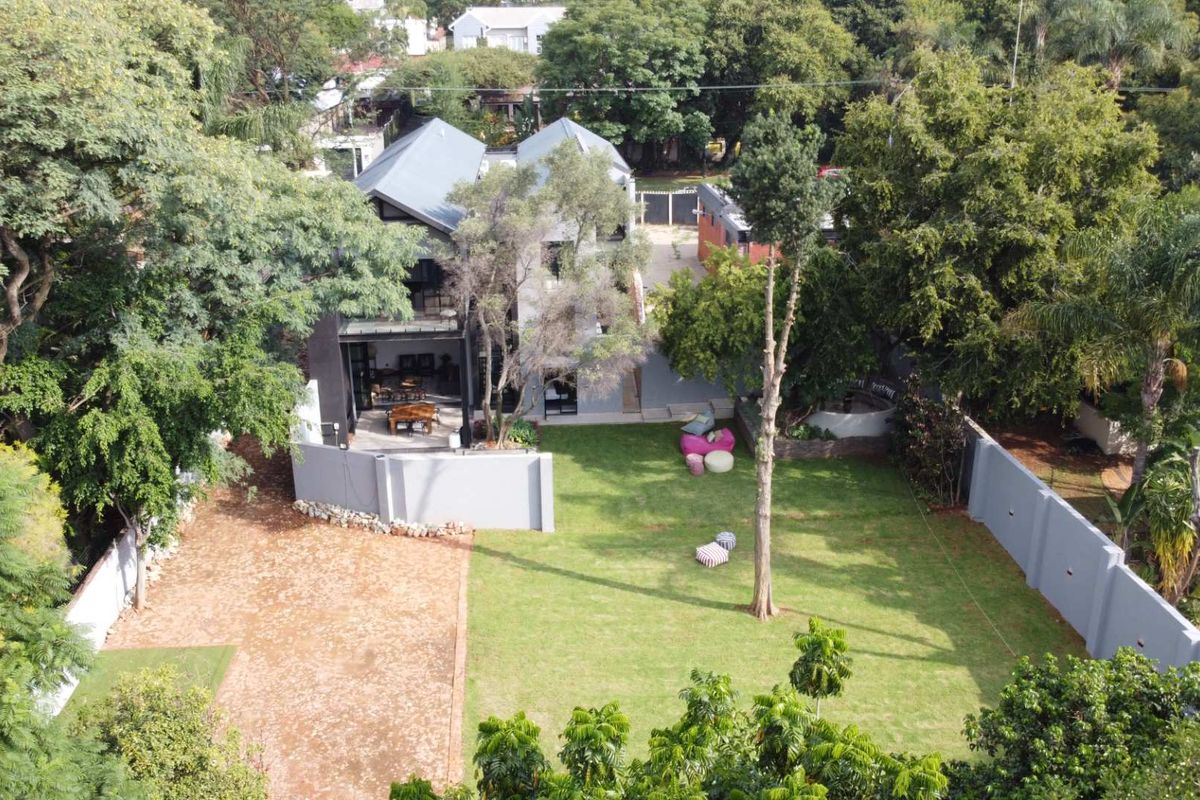 Aerial view of a residential property featuring a spacious lawn, mature trees, perimeter walling, and a rear patio area.