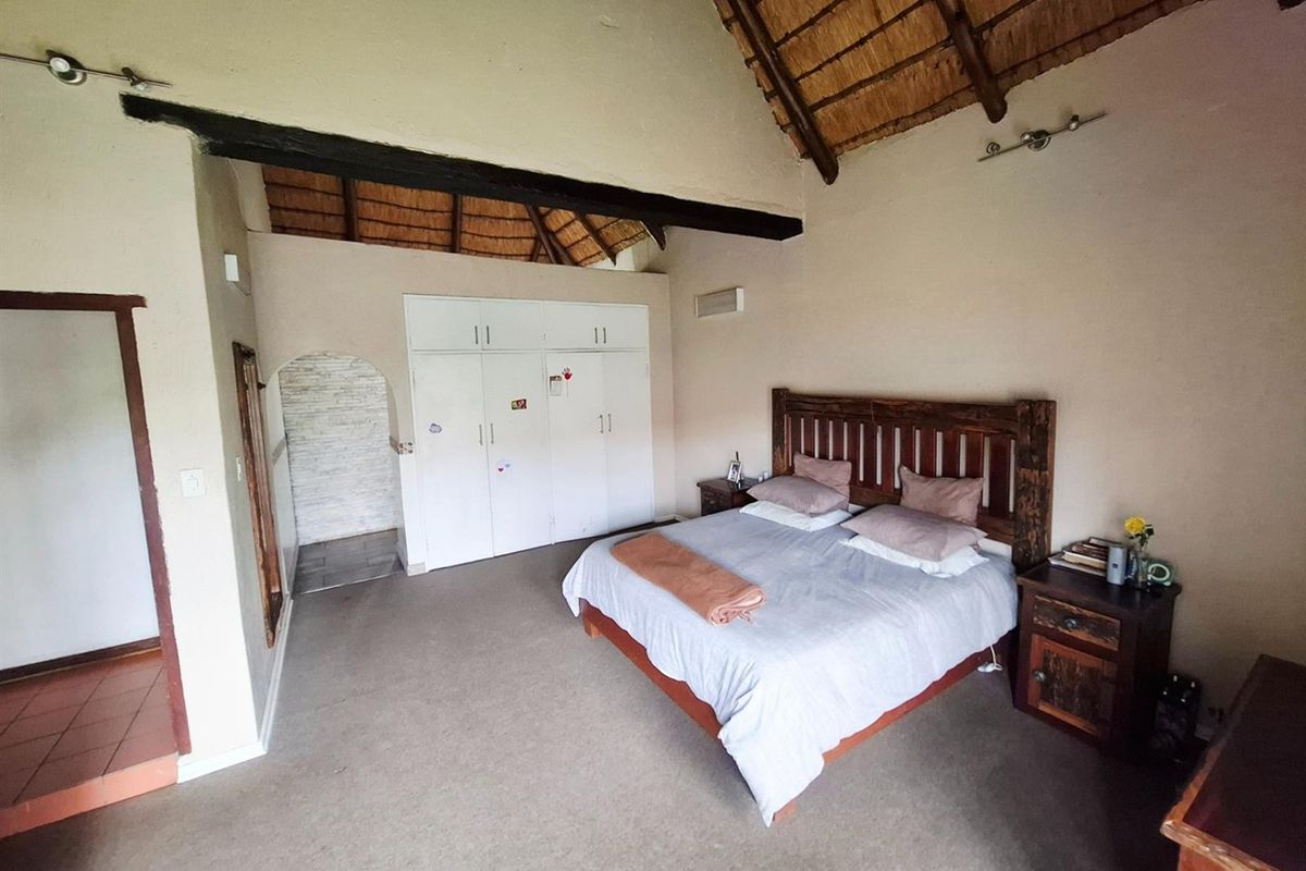Spacious bedroom featuring a high vaulted thatched ceiling with exposed timber beams, built-in storage, and an arched entry to an adjoining area.
