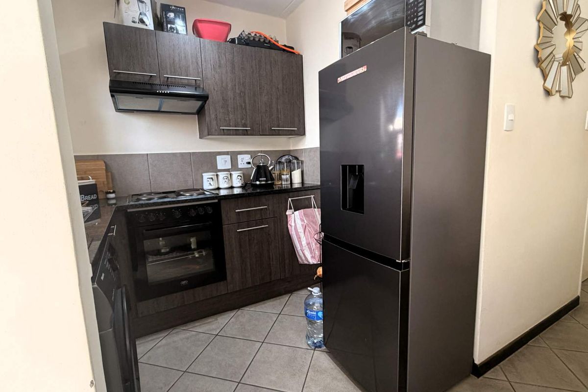 Compact kitchen featuring dark wood cabinetry, granite countertops, tiled backsplash, and built-in oven with extractor fan.