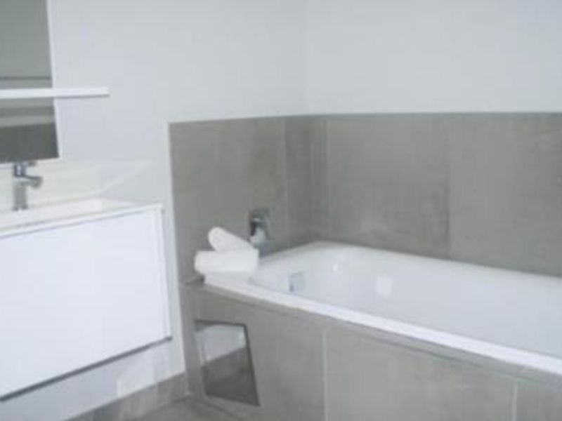 Modern bathroom featuring a wall-mounted vanity with basin, mirror, and a tiled bathtub area with neutral finishes.
