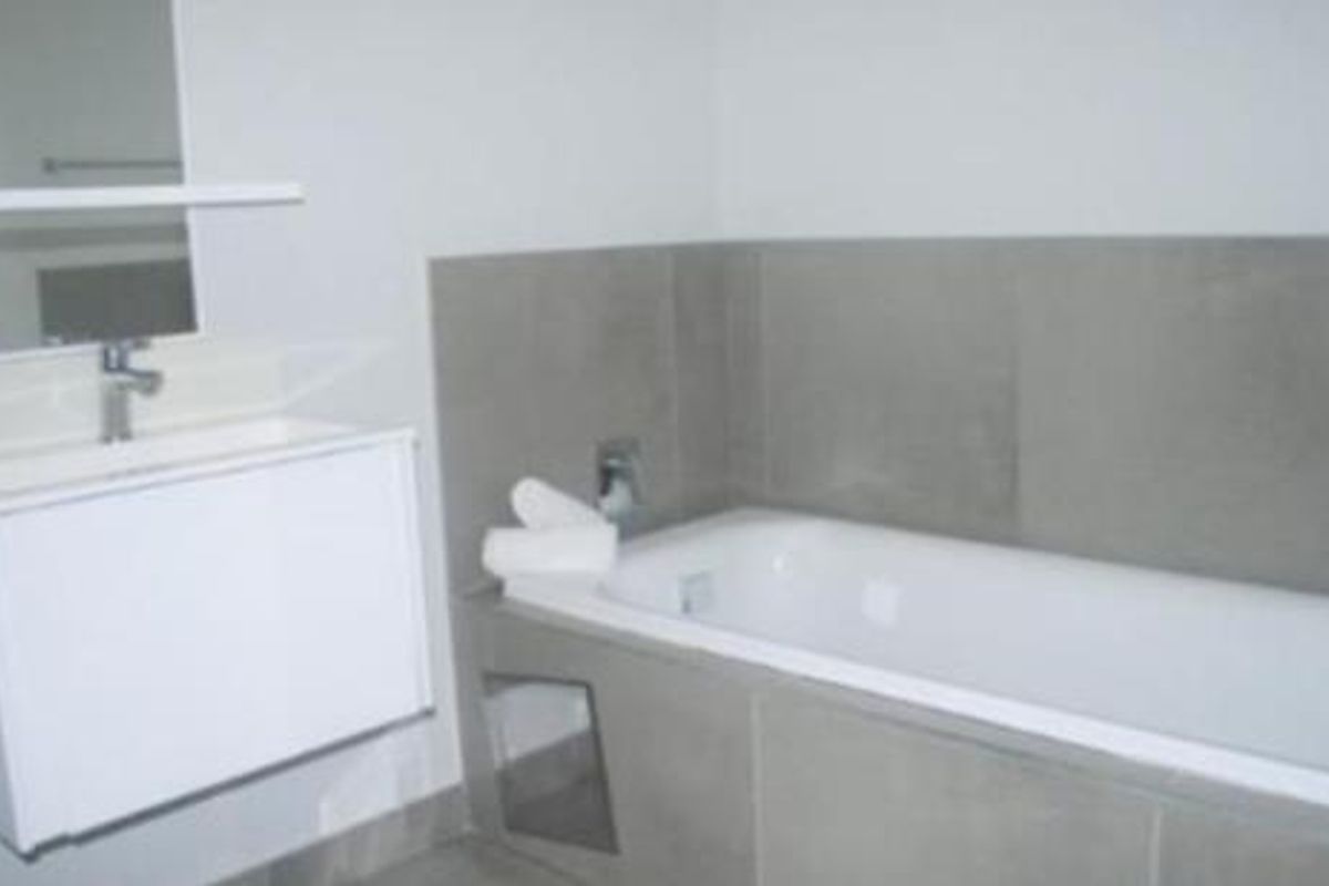 Modern bathroom featuring a wall-mounted vanity with basin, mirror, and a tiled bathtub area with neutral finishes.