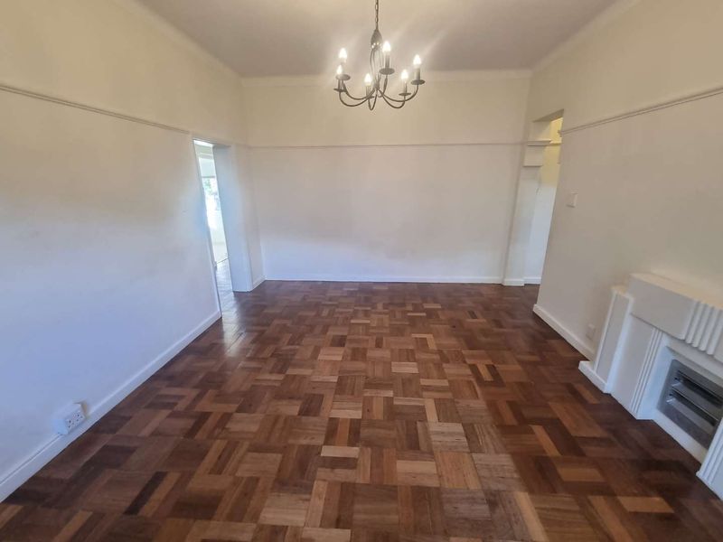 A spacious, empty living room featuring classic parquet flooring, a built-in fireplace, and a decorative ceiling chandelier, offering a bright and neutral living space.