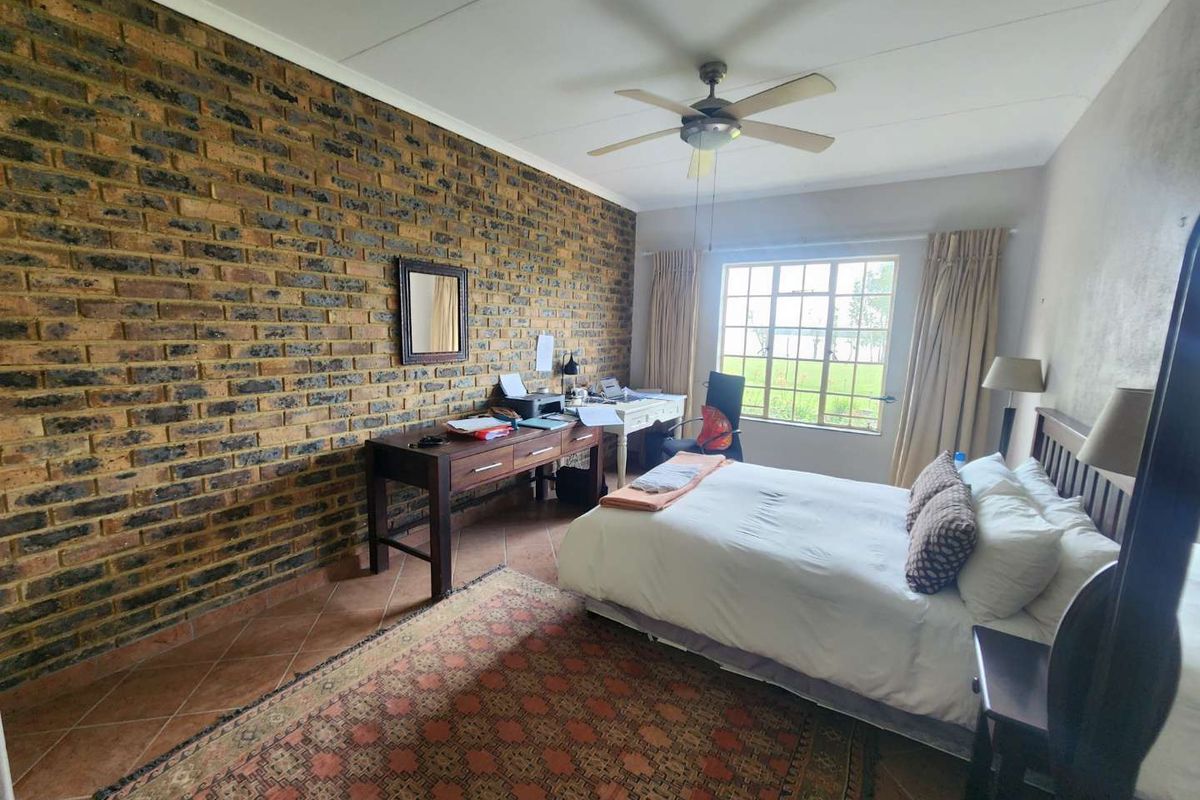 A spacious bedroom featuring a distinctive exposed brick feature wall, tiled flooring, and a ceiling fan, offering a comfortable and well-lit living space.