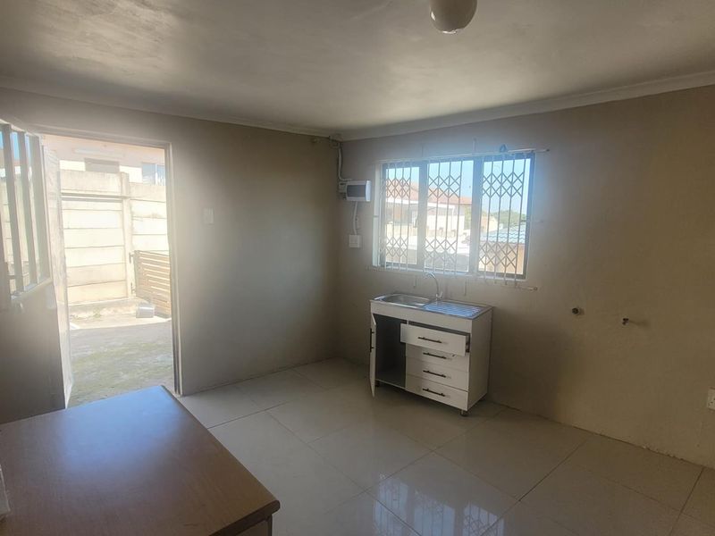 A basic kitchen area featuring tiled flooring, a single stainless steel sink unit, and direct access to the exterior through a security door.