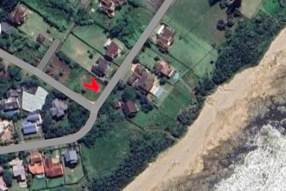 An aerial view of a vacant residential plot situated in a coastal neighborhood, highlighting its proximity to the beach and surrounding properties.