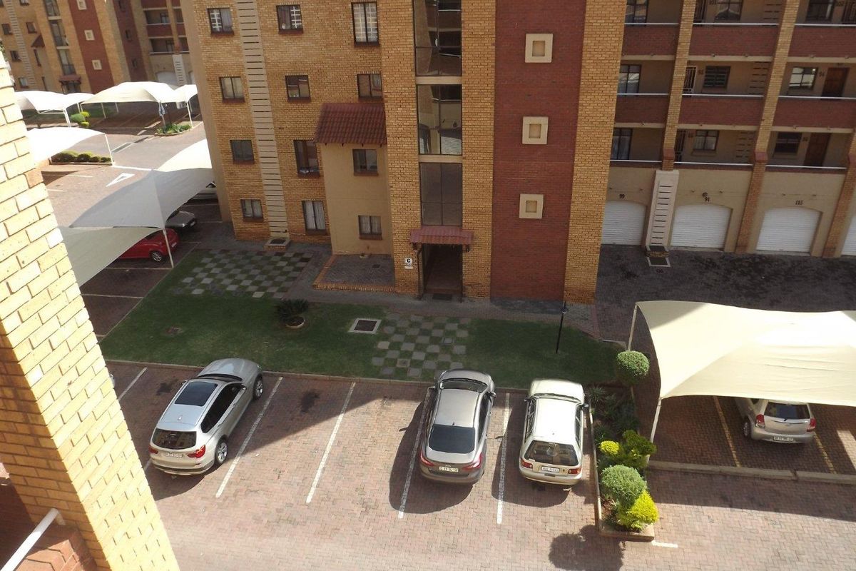 An elevated aerial view of an apartment complex courtyard featuring paved parking bays, shade cloth carports, and landscaped garden areas.