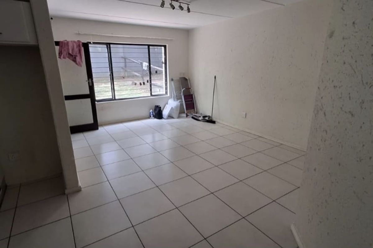 An empty living room featuring tiled flooring, textured walls, and a large metal-framed window providing natural light.