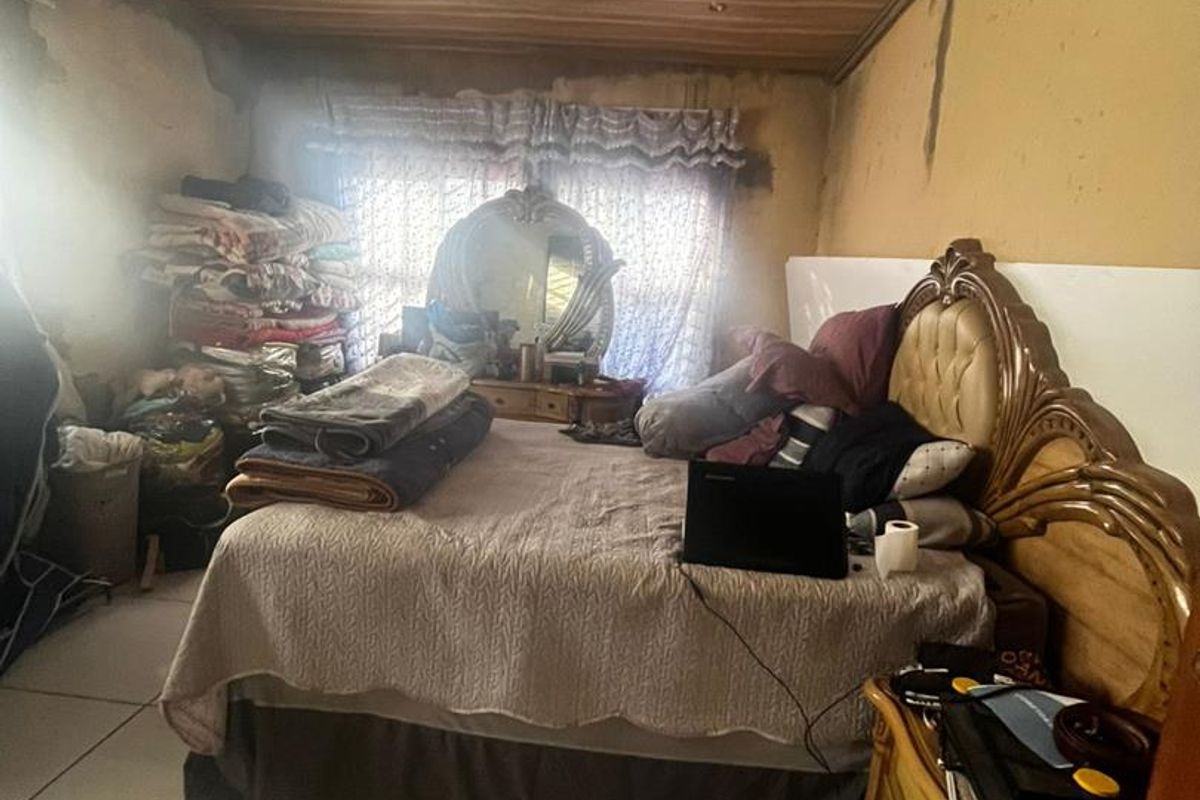 A bedroom featuring tiled flooring and a decorative wood-paneled ceiling, currently showing significant signs of wear and wall damage.