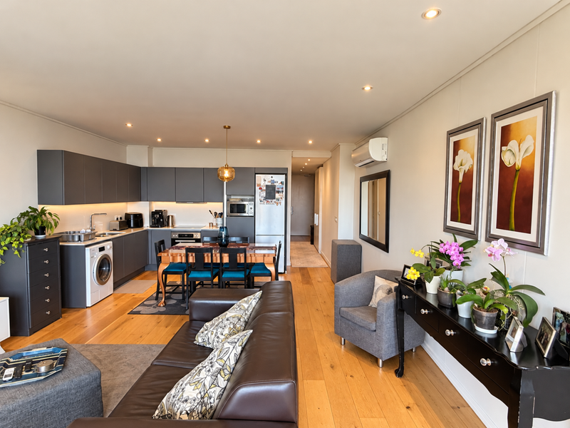 Modern open-plan living area featuring hardwood flooring, recessed lighting, and a sleek kitchen with integrated appliances and contemporary cabinetry.