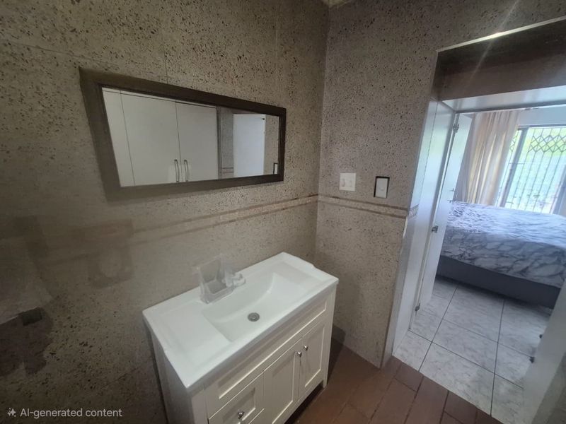 A bathroom vanity area featuring a modern white cabinet with an integrated basin and a wall-mounted mirror, set against textured tiled walls.