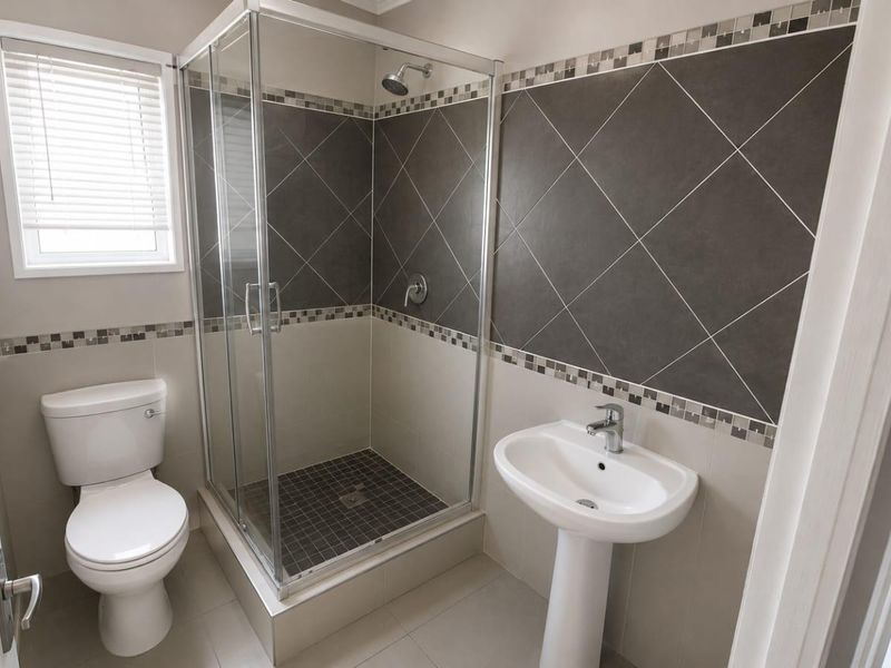 A clean and well-maintained bathroom featuring a pedestal sink, a glass-enclosed shower with dark tiled accents, and a standard toilet.