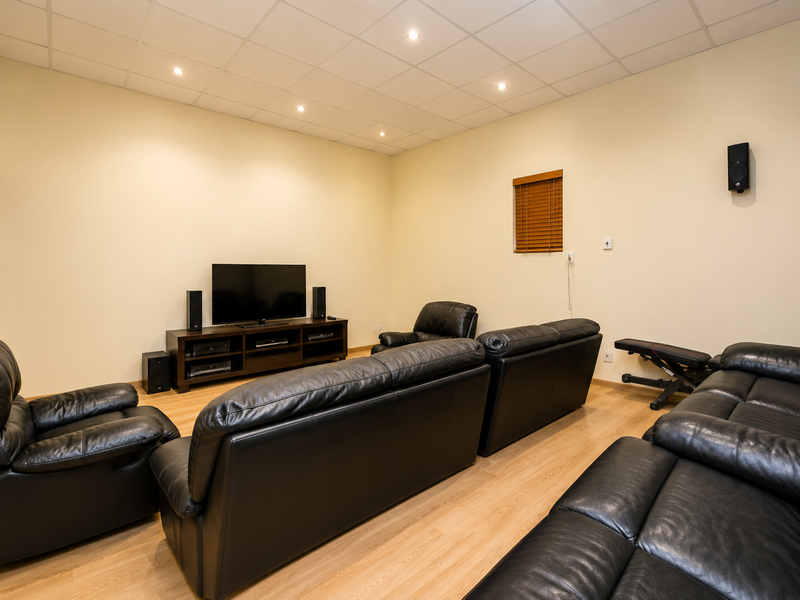 A dedicated cinema room featuring a suspended ceiling with recessed lighting, laminate flooring, and timber window blinds.