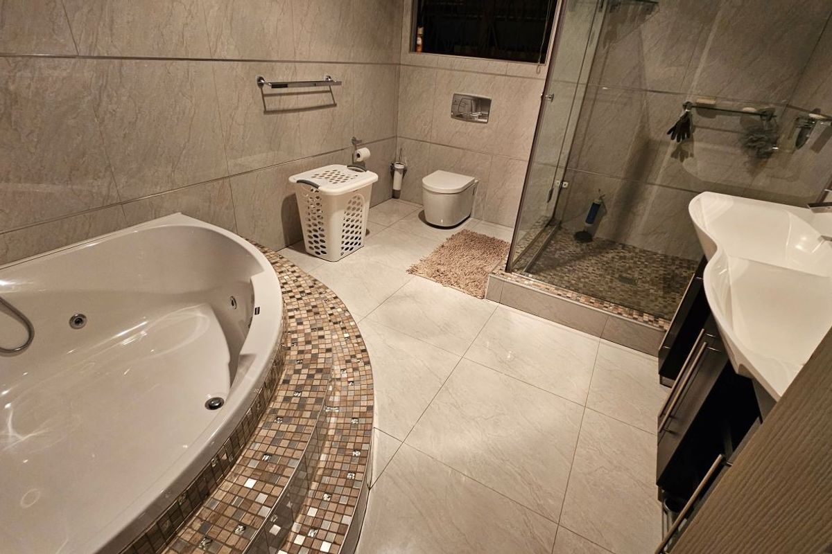 Modern bathroom featuring a built-in jetted bathtub, glass-enclosed shower, wall-mounted toilet, and a double vanity with contemporary tiled finishes.