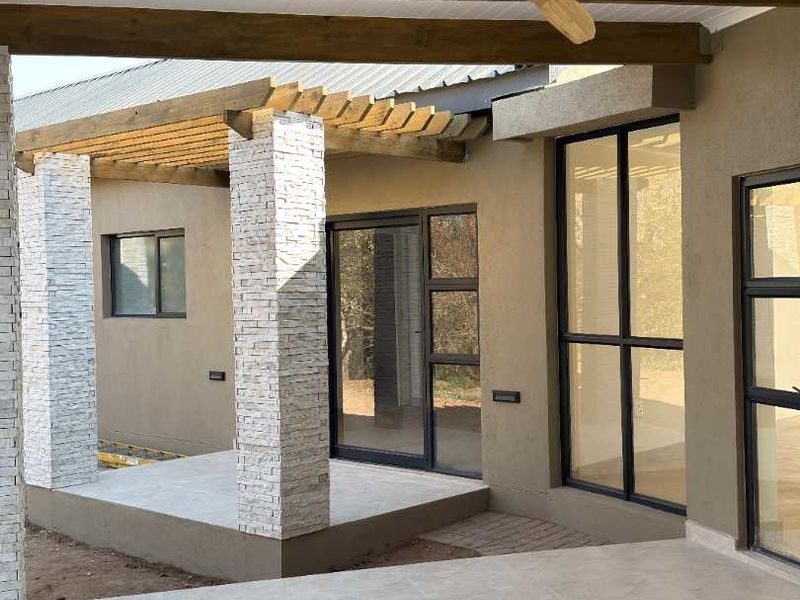 A modern covered patio featuring exposed timber beams, a ceiling fan, stone-clad pillars, and large aluminium-framed glass doors leading into the home.