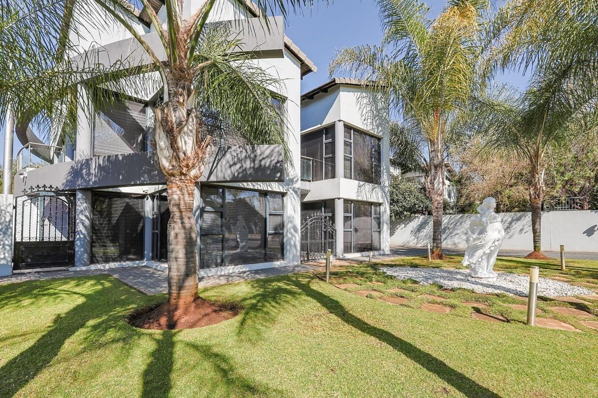 Modern multi-story residential exterior featuring large glass windows, metal balcony railings, and a well-maintained landscaped garden with mature palm trees.