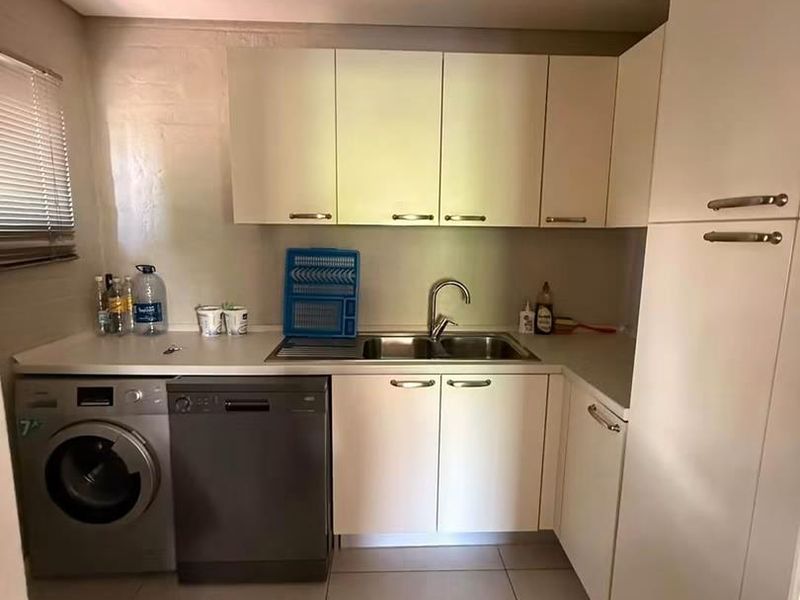 A functional kitchen featuring built-in cabinetry, laminate countertops, a stainless steel double sink, and tiled flooring with space for integrated appliances.