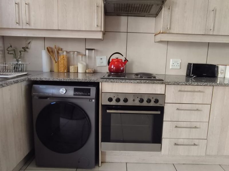 A functional kitchen featuring light wood-look laminate cabinetry, granite countertops, a built-in oven with hob, and a tiled backsplash.
