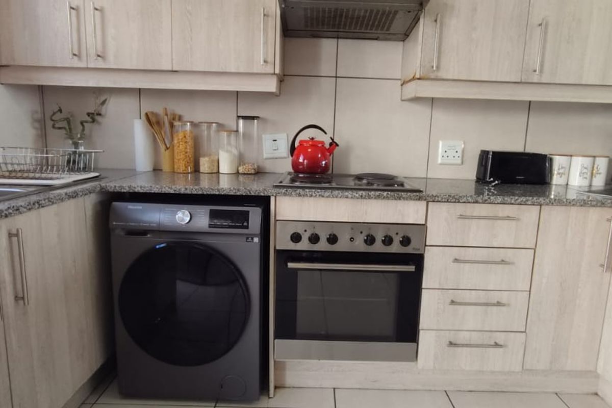 A functional kitchen featuring light wood-look laminate cabinetry, granite countertops, a built-in oven with hob, and a tiled backsplash.