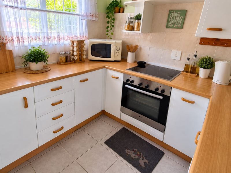 A well-maintained kitchen featuring white cabinetry, light wood-look laminate countertops, a built-in oven with electric hob, and neutral tiled flooring.