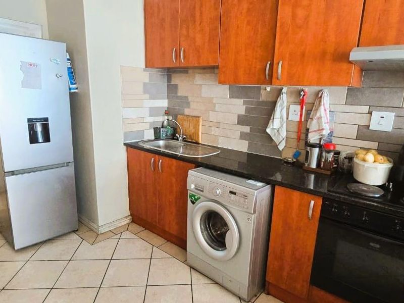 A functional kitchen featuring wooden cabinetry, granite countertops, a tiled backsplash, and integrated appliances including an oven, hob, and extractor fan.