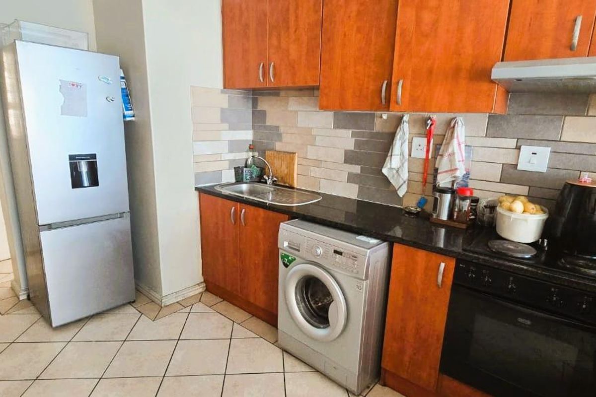 A functional kitchen featuring wooden cabinetry, granite countertops, a tiled backsplash, and integrated appliances including an oven, hob, and extractor fan.