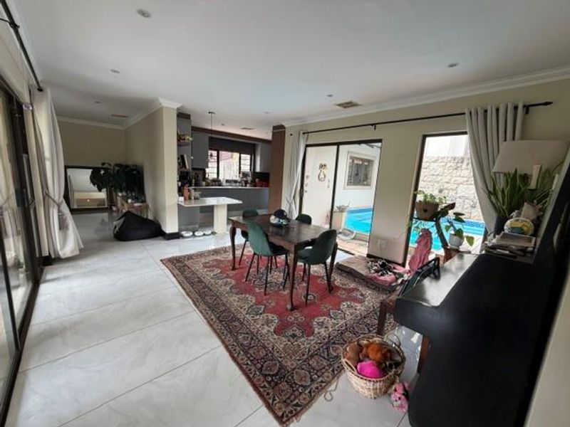 Spacious open-plan living and dining area featuring large format floor tiles, recessed lighting, and seamless flow to the outdoor patio and pool area.