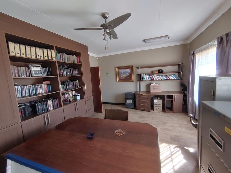 A functional home office featuring extensive built-in wooden cabinetry, shelving units, a built-in desk, and a ceiling fan.