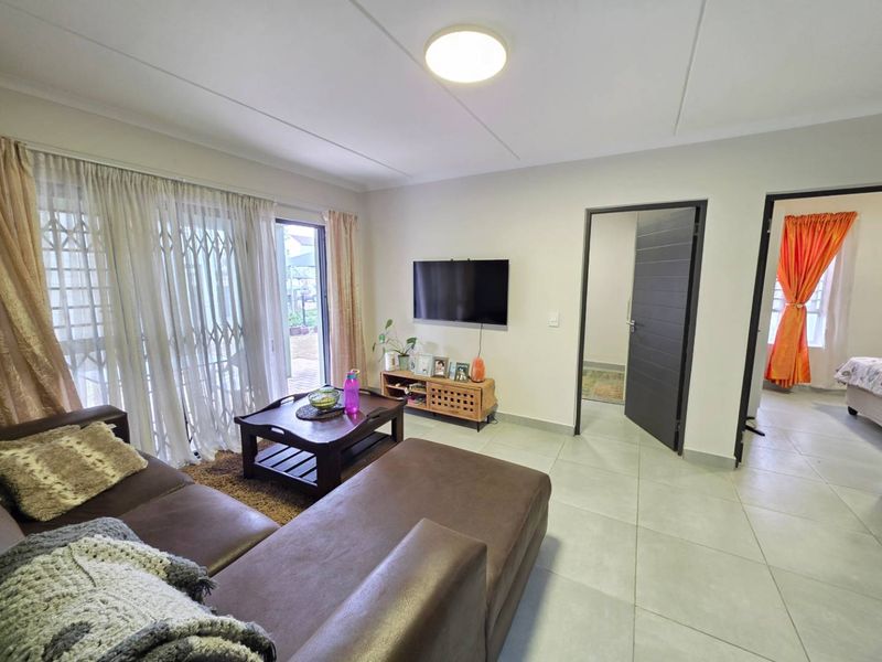 A well-maintained living room featuring neutral tiled flooring, a sliding glass door with security gate, and direct access to adjacent rooms.