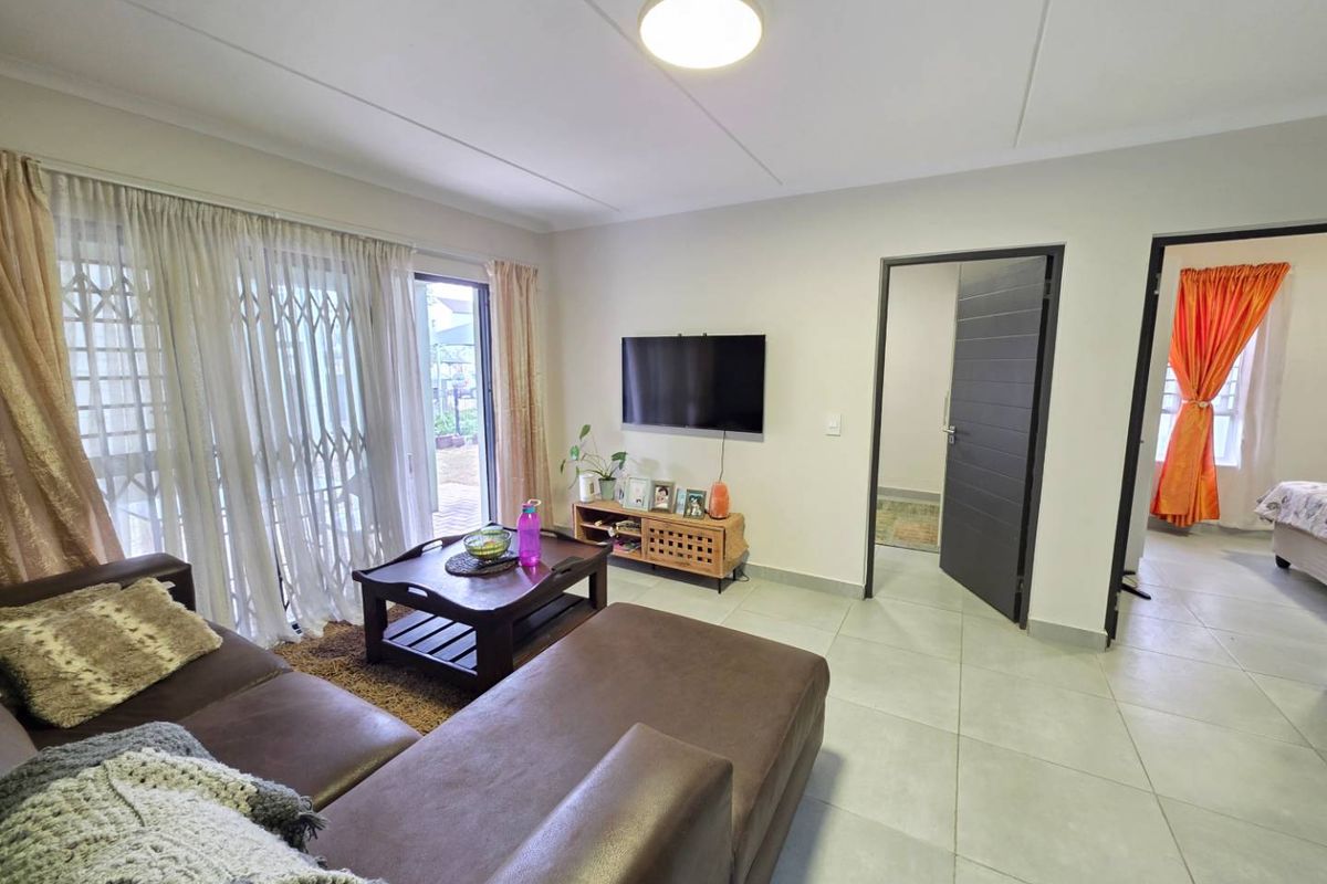 A well-maintained living room featuring neutral tiled flooring, a sliding glass door with security gate, and direct access to adjacent rooms.
