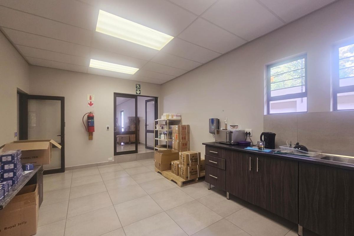 A functional kitchenette area featuring dark cabinetry, tiled flooring, and a drop ceiling with integrated lighting, suitable for office or commercial use.