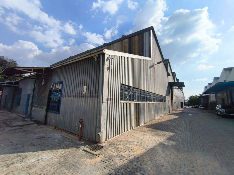 Exterior view of an industrial warehouse building featuring corrugated metal cladding, steel-framed windows, and paved access area.