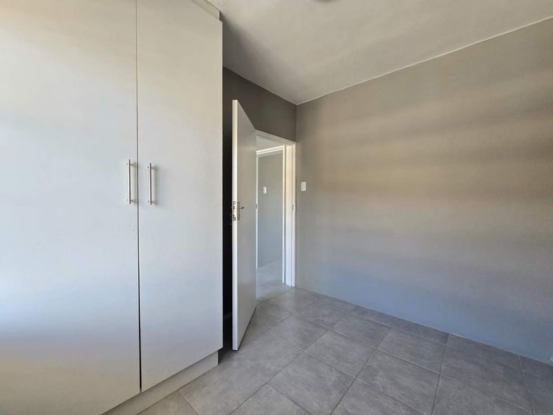 A clean, empty bedroom featuring neutral grey walls, tiled flooring, and a built-in white wardrobe with modern handles.