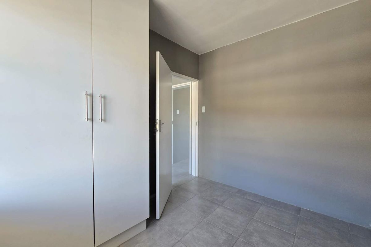 A clean, empty bedroom featuring neutral grey walls, tiled flooring, and a built-in white wardrobe with modern handles.