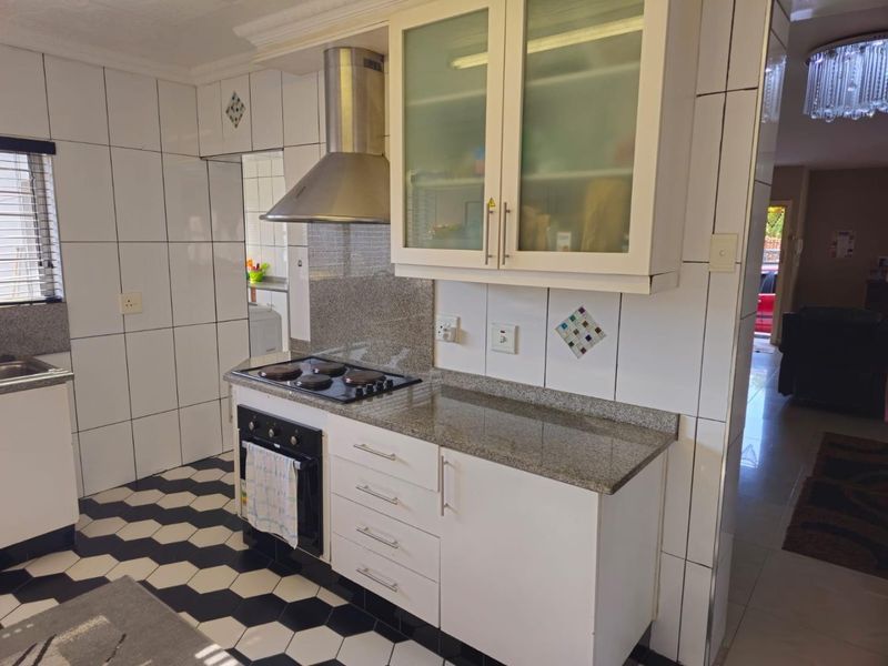 Functional kitchen featuring granite countertops, built-in oven, electric hob, stainless steel extractor fan, and ample cabinetry with a tiled finish.