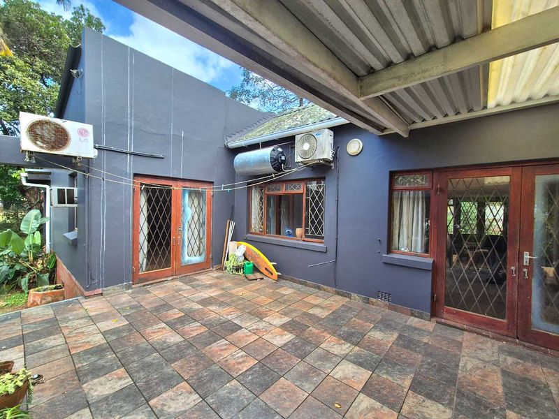A covered outdoor patio area featuring tiled flooring, external air conditioning units, and direct access to the home through timber-framed doors.