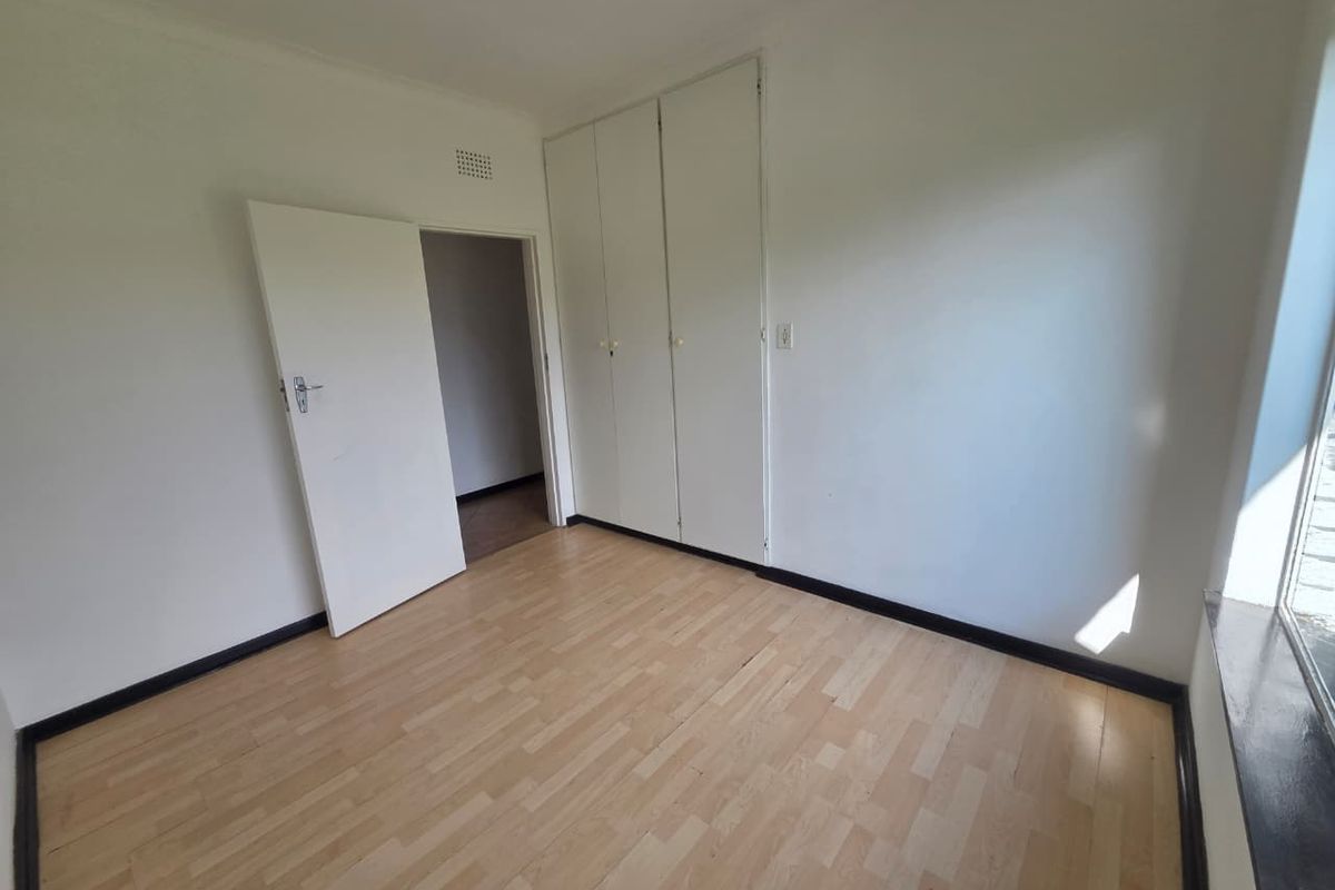 An empty bedroom featuring light-toned laminate flooring and built-in storage cupboards.