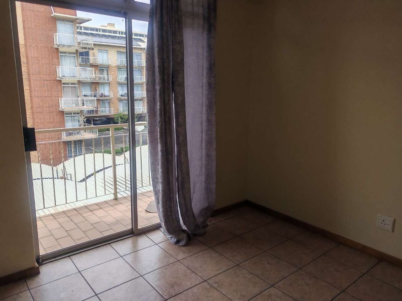 An empty bedroom featuring tiled flooring and a sliding glass door that provides access to a private balcony.