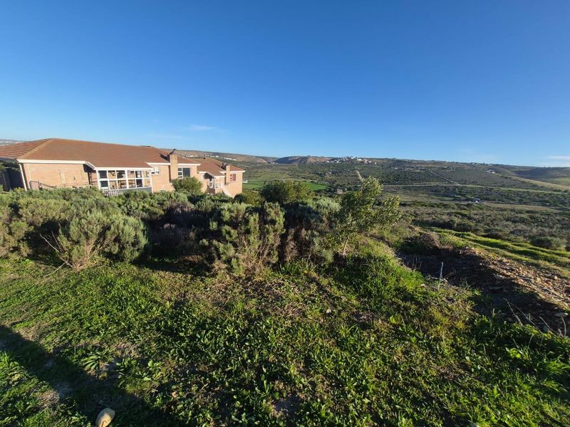 A wide-angle view of the vacant residential land featuring natural vegetation, sloped terrain, and a scenic outlook over the surrounding landscape.