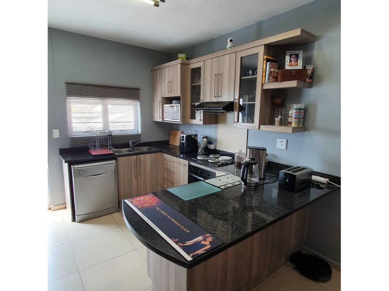 A functional kitchen featuring wood-look laminate cabinetry, dark granite countertops, built-in oven, extractor fan, and tiled flooring with a breakfast nook extension.