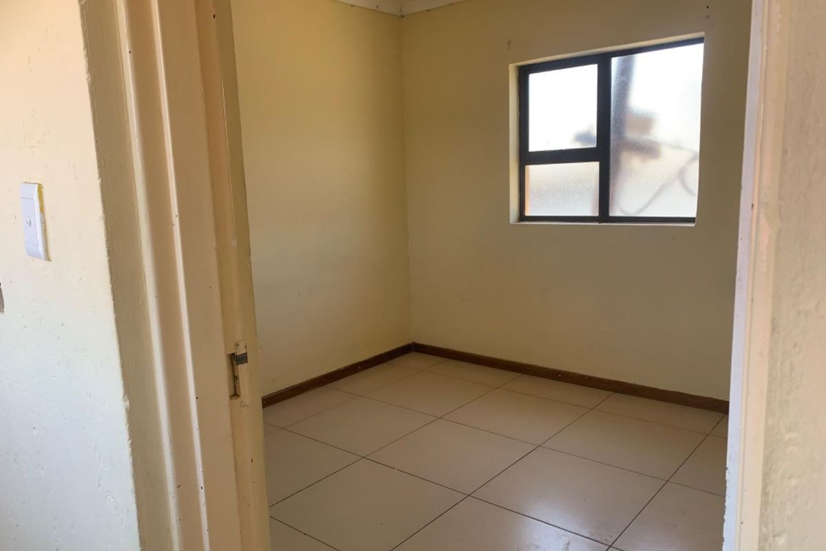 A vacant bedroom featuring neutral tiled flooring and a single window, offering a blank canvas for potential renovation or interior design updates.