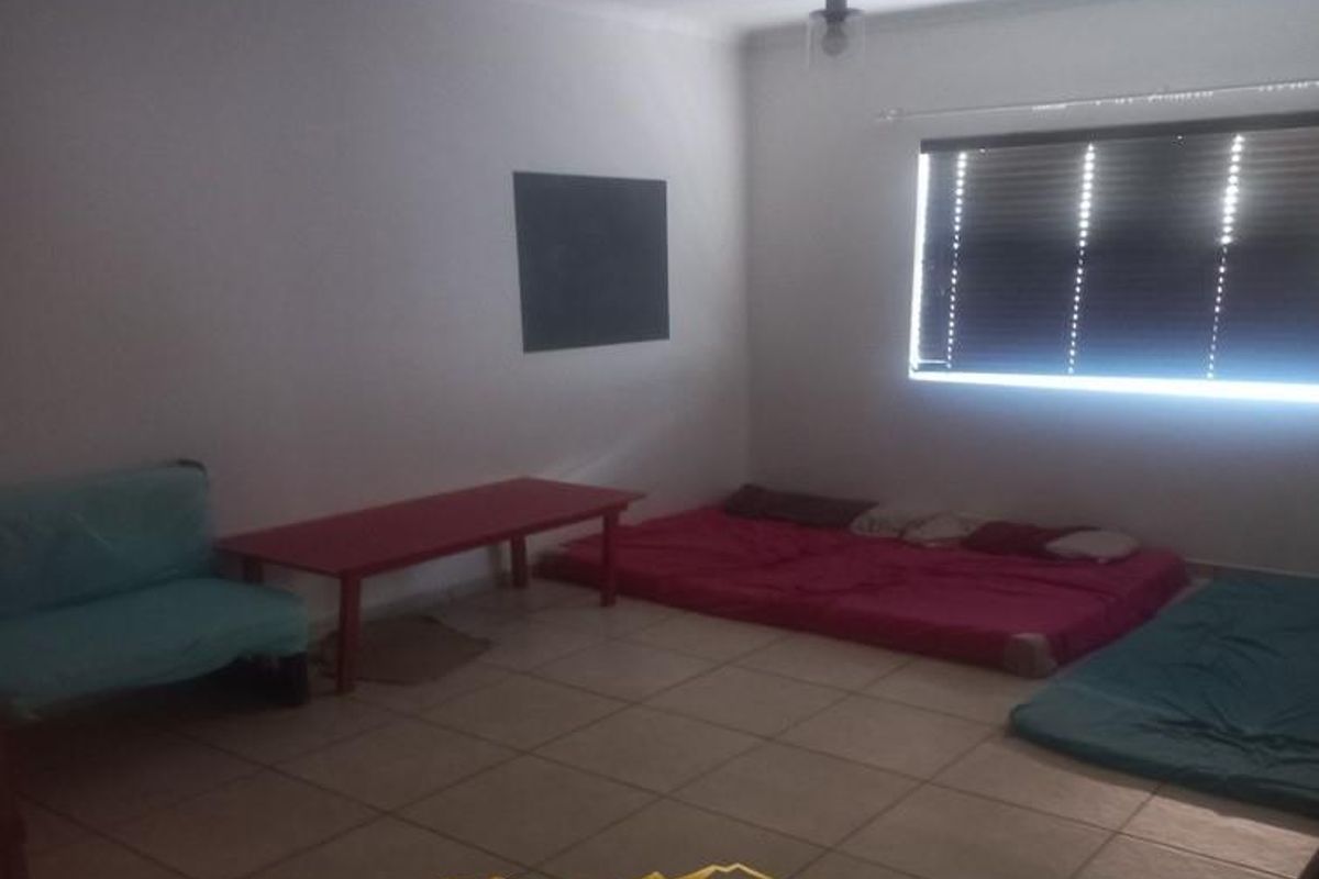 A spacious bedroom featuring tiled flooring and a window with fitted blinds, offering a blank canvas for interior design.