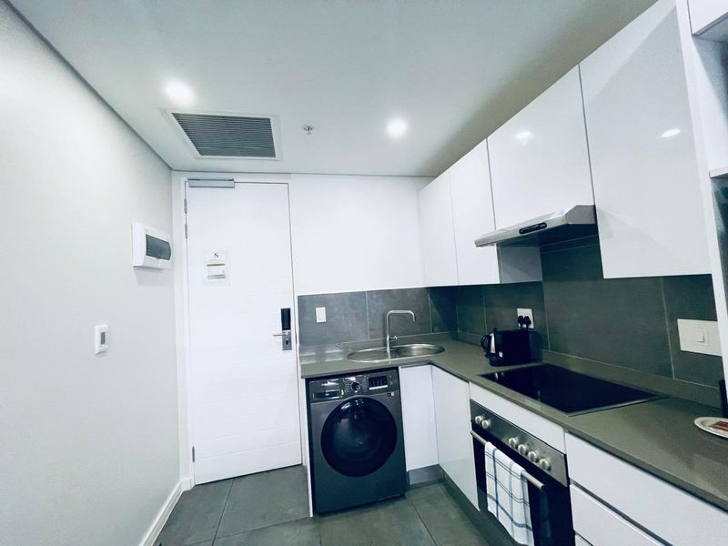 Modern compact kitchen featuring white cabinetry, stone countertops, integrated appliances, and a sleek tiled backsplash in a contemporary apartment setting.