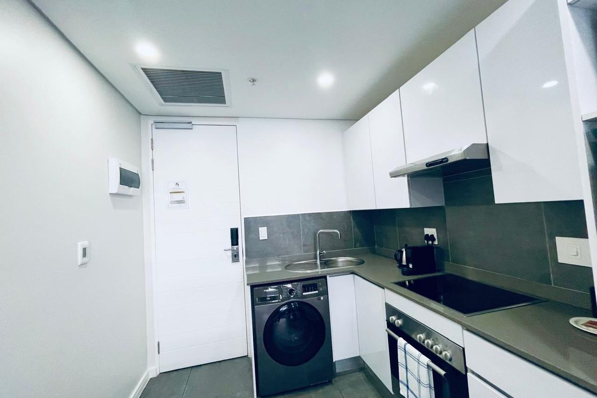 Modern compact kitchen featuring white cabinetry, stone countertops, integrated appliances, and a sleek tiled backsplash in a contemporary apartment setting.