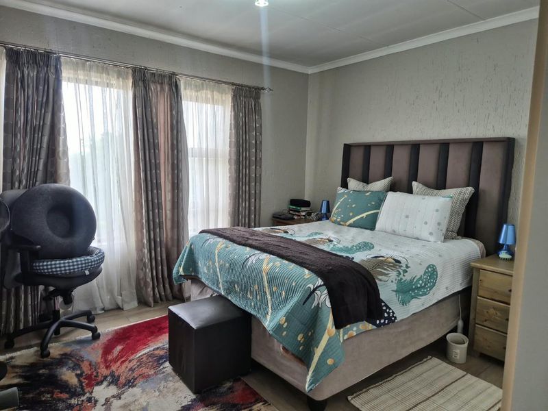 A well-lit bedroom featuring textured walls, coving, and large windows with curtain tracks, providing a comfortable and functional living space.