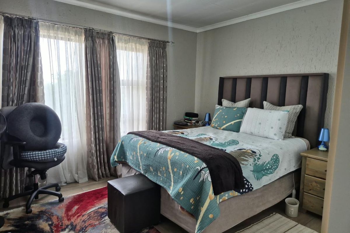 A well-lit bedroom featuring textured walls, coving, and large windows with curtain tracks, providing a comfortable and functional living space.