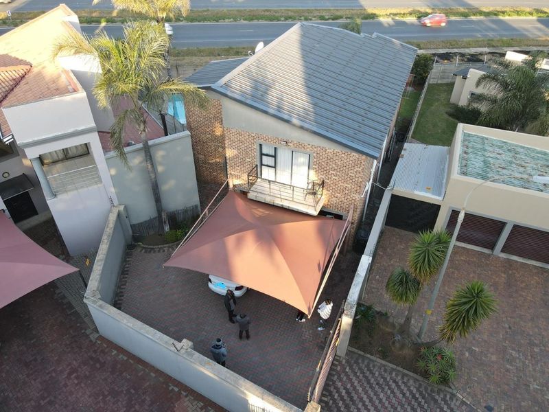 Aerial view of the property featuring a paved driveway with a shade sail, brick exterior, and a small balcony.