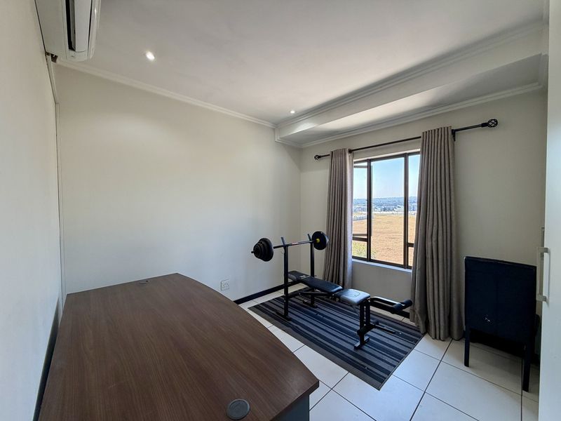 A bright, functional office space featuring tiled flooring, recessed lighting, and a split-system air conditioner, offering a clear view through the window.