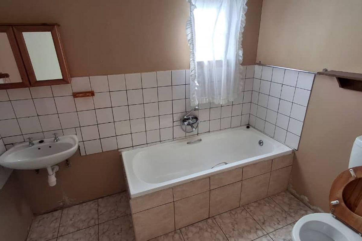 A dated bathroom featuring a standard bathtub, wall-mounted basin, and toilet, with tiled splashbacks and flooring in need of modernization.