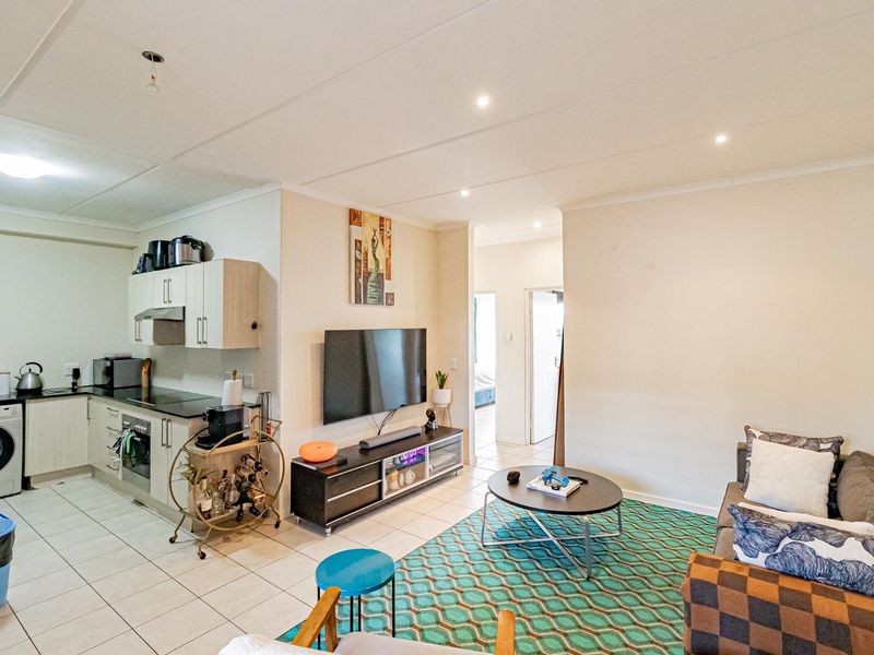 Open-plan living area featuring a compact kitchen with built-in cabinetry, electric hob, and oven, seamlessly flowing into the lounge space with tiled flooring throughout.